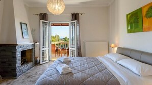 A bedroom with a large bed, a fireplace, and a balcony with a view. - Villa Maxim with Private Pool & Tennis Court (Corfu)