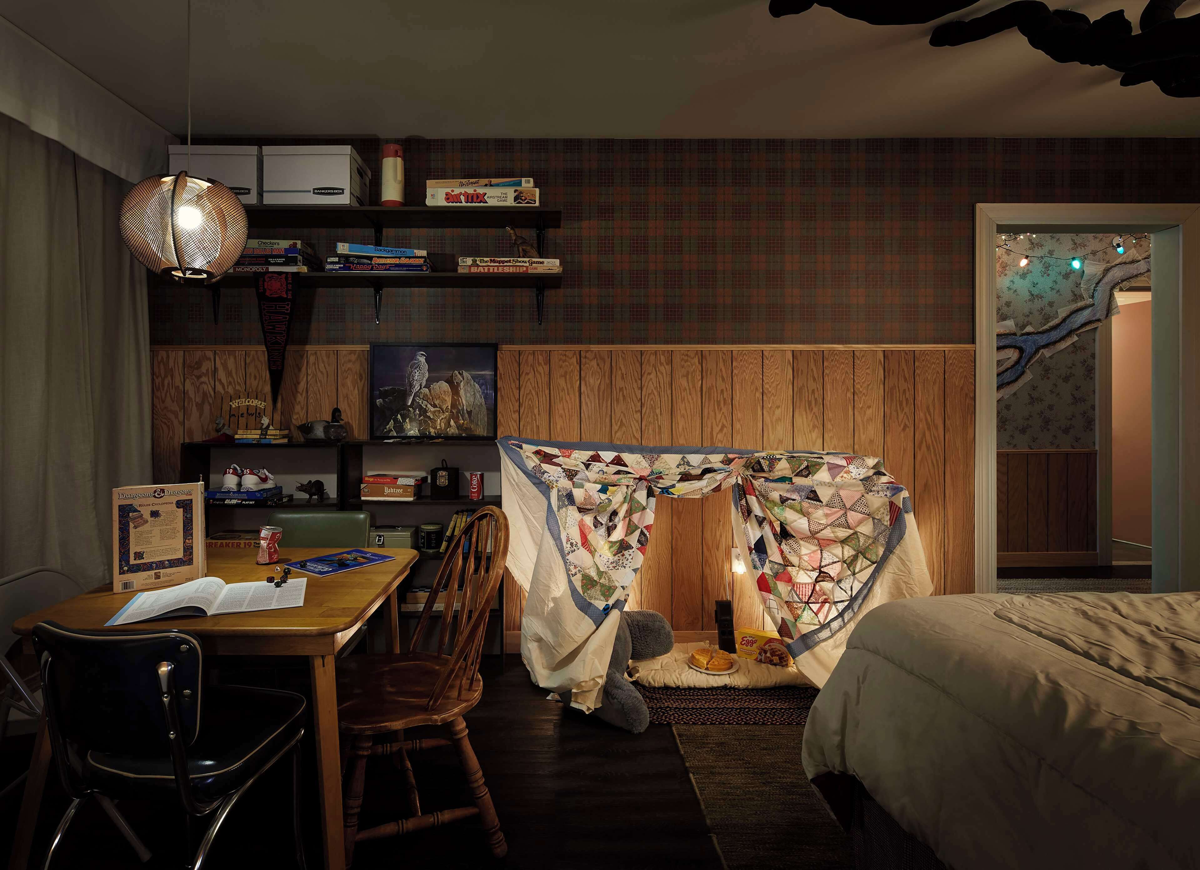 A cozy bedroom with a bed, a desk with a chair, a bookshelf, and a quilted tent-like structure.