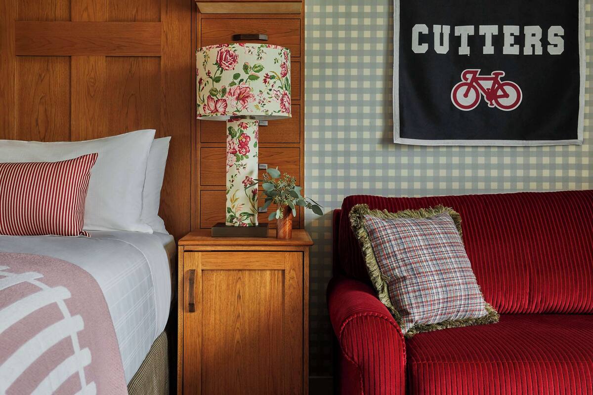 A hotel room with a wooden headboard, a red sofa, a wooden nightstand with a lamp, and a wall with a 'CUTTERS' sign.