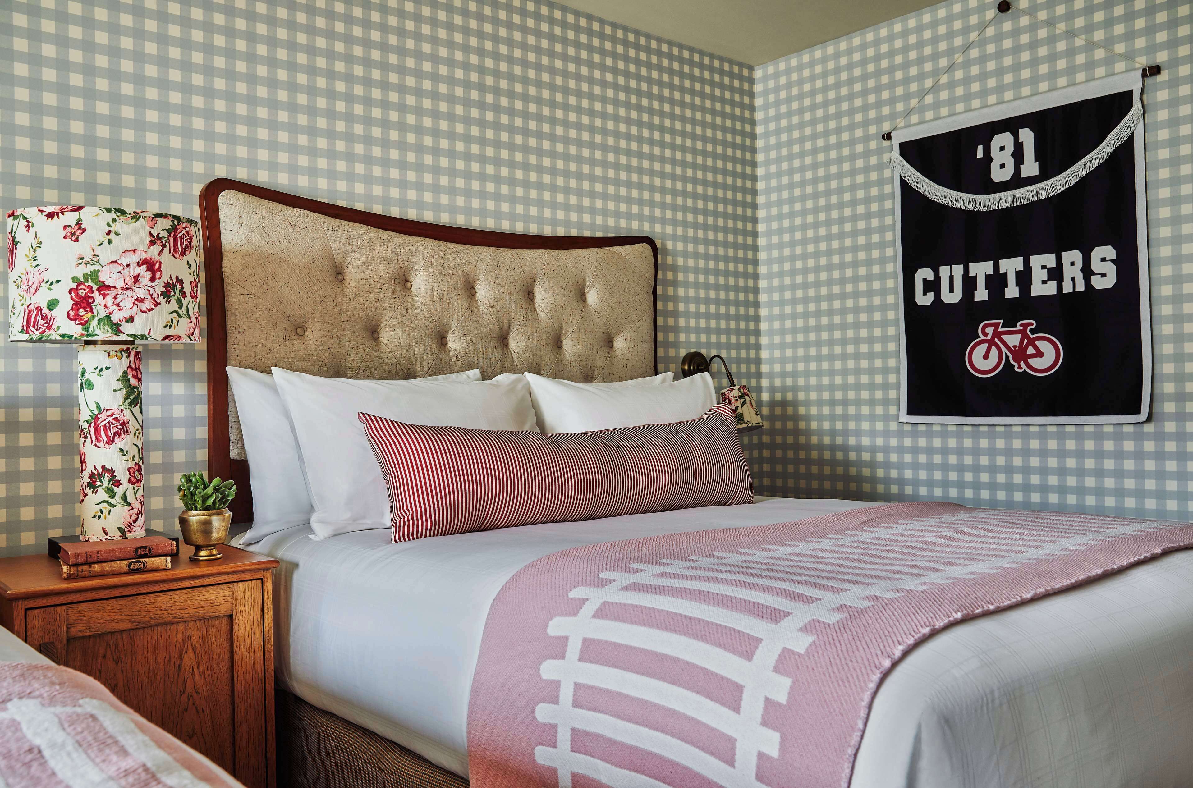 A neatly made bed with a striped pillow, a floral lamp, and a framed '81 Cutters' banner on the wall.