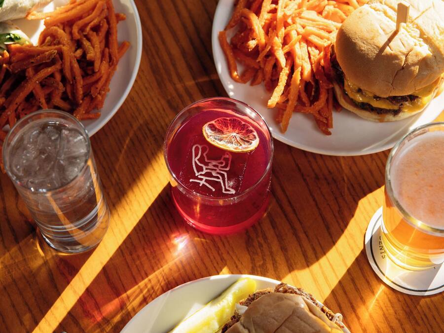 Et træbord med et måltid bestående af en burger, pommes frites og en drik.