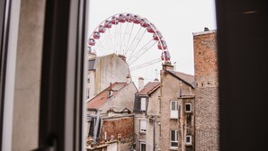 A view of a Ferris wheel from a window overlooking a narrow street with brick buildings. - Hotel des Arcades (Reims)