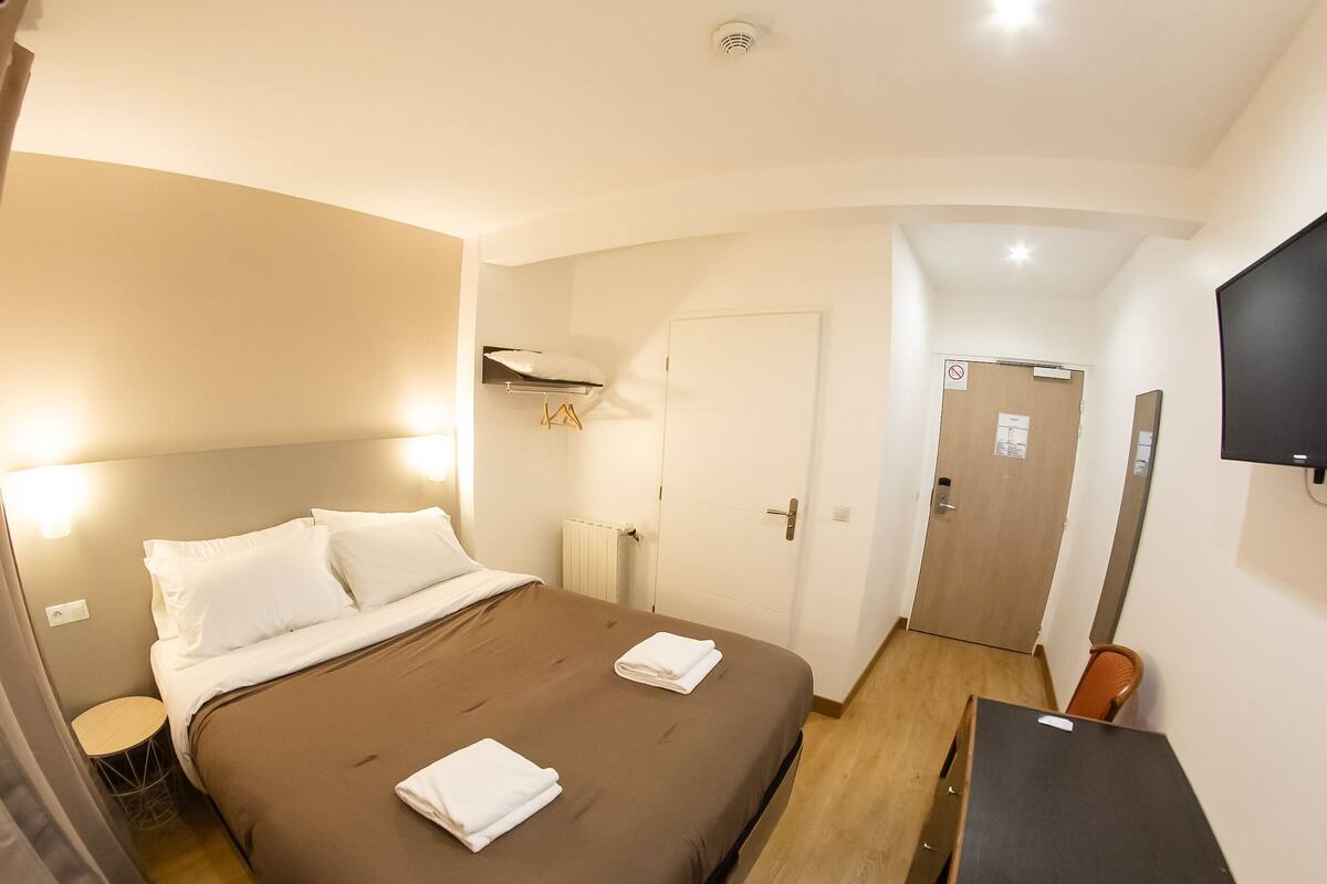 A hotel room with a bed, bedside table, TV, and a door.