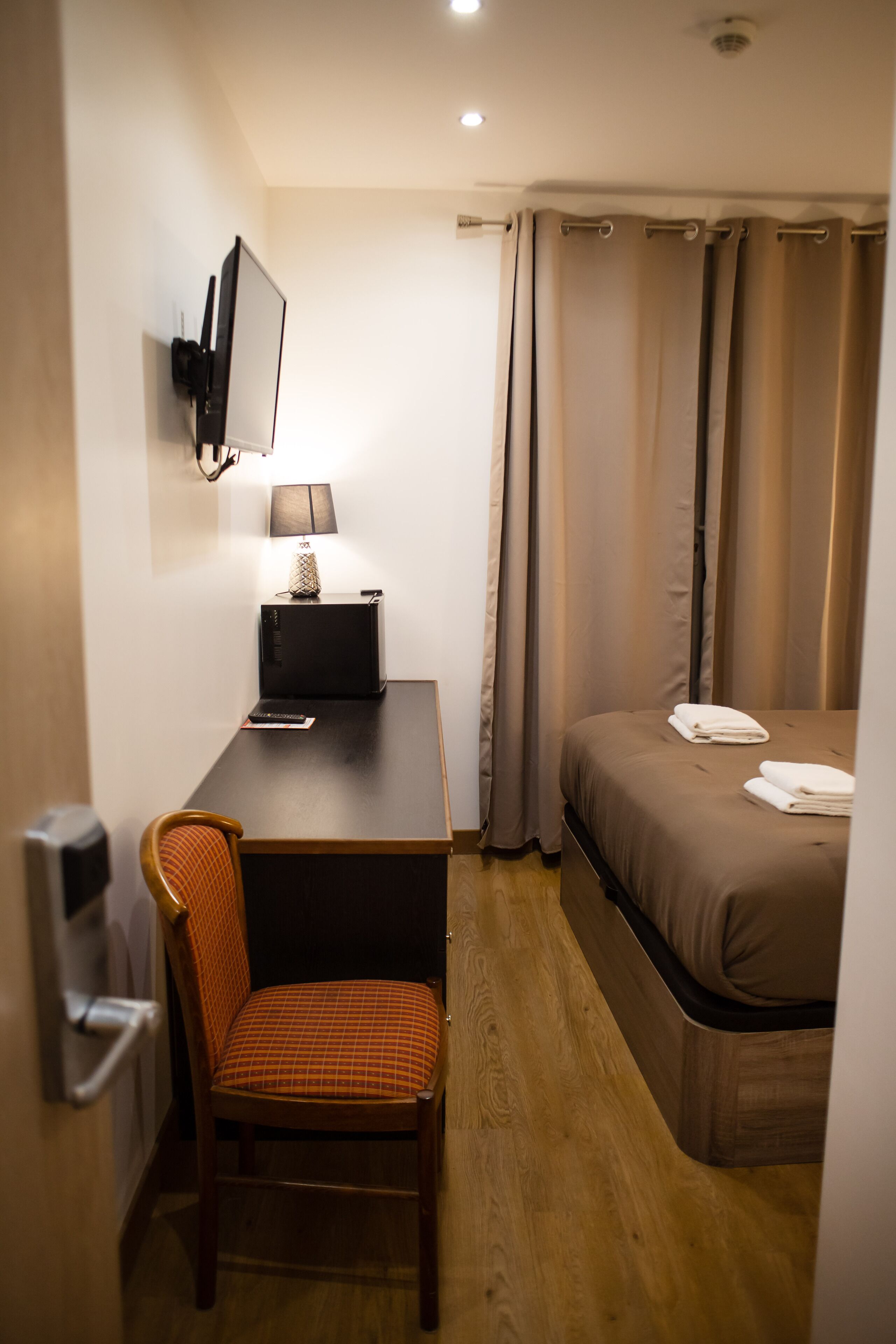Una habitación de hotel con una cama, un escritorio con silla, un televisor y una lámpara.