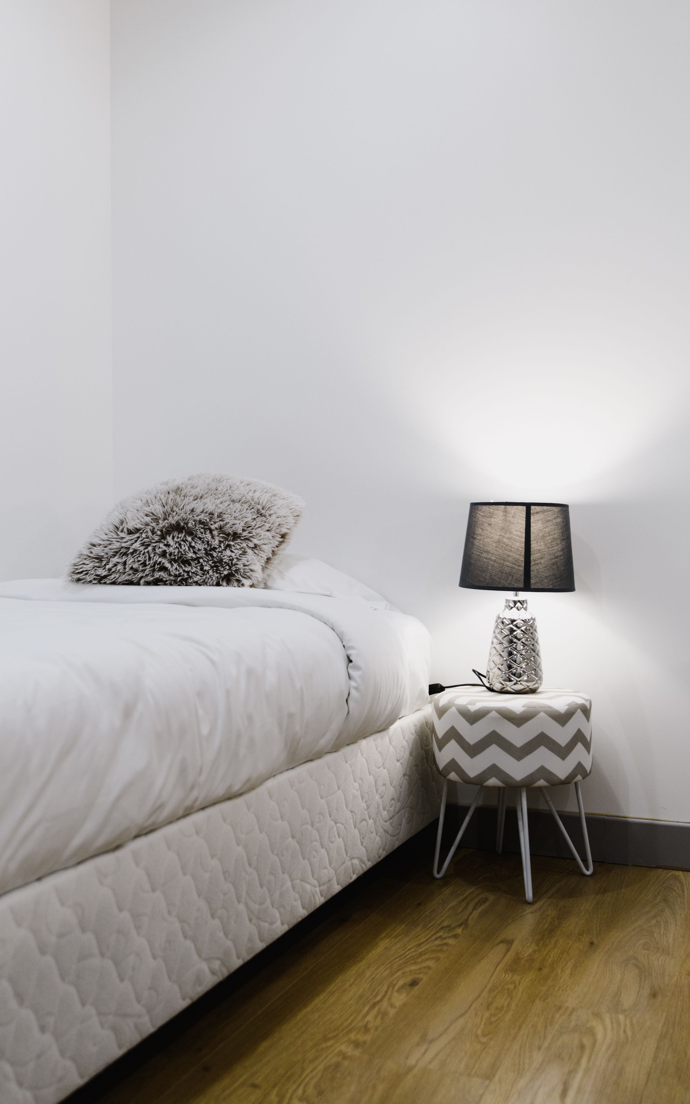 Un lit bien fait, avec un oreiller moelleux, une petite table de chevet surmontée d’une lampe et un plancher en bois.
