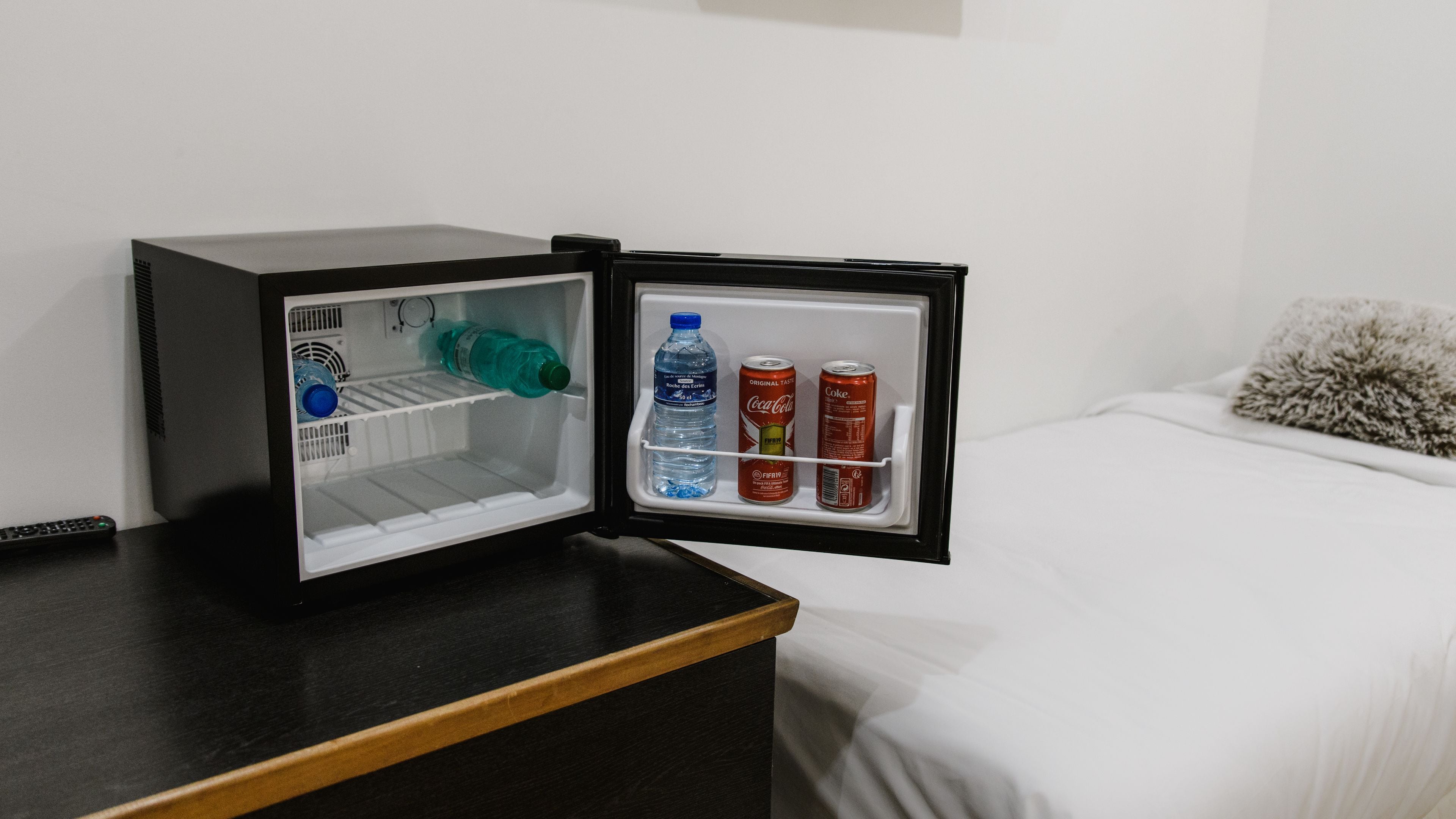 A small black refrigerator with a water bottle and two cans of soda on the door shelf.