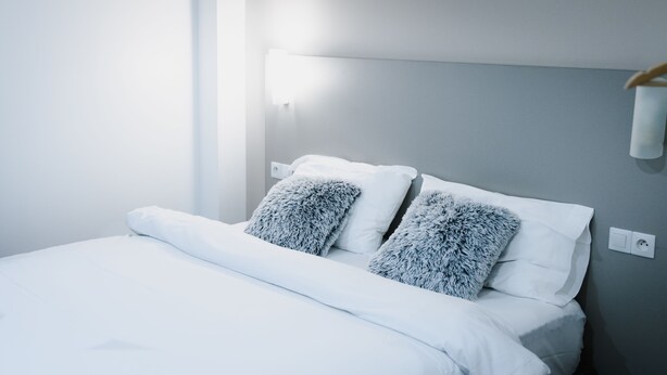 A neatly made bed with white linens and two fluffy pillows. - Hotel des Arcades (Reims)