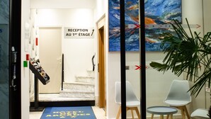 A hotel reception area with a reception desk, a blue carpet with 'HOTEL' text, a staircase, and a large painting on the wall. - Hotel des Arcades (Reims)