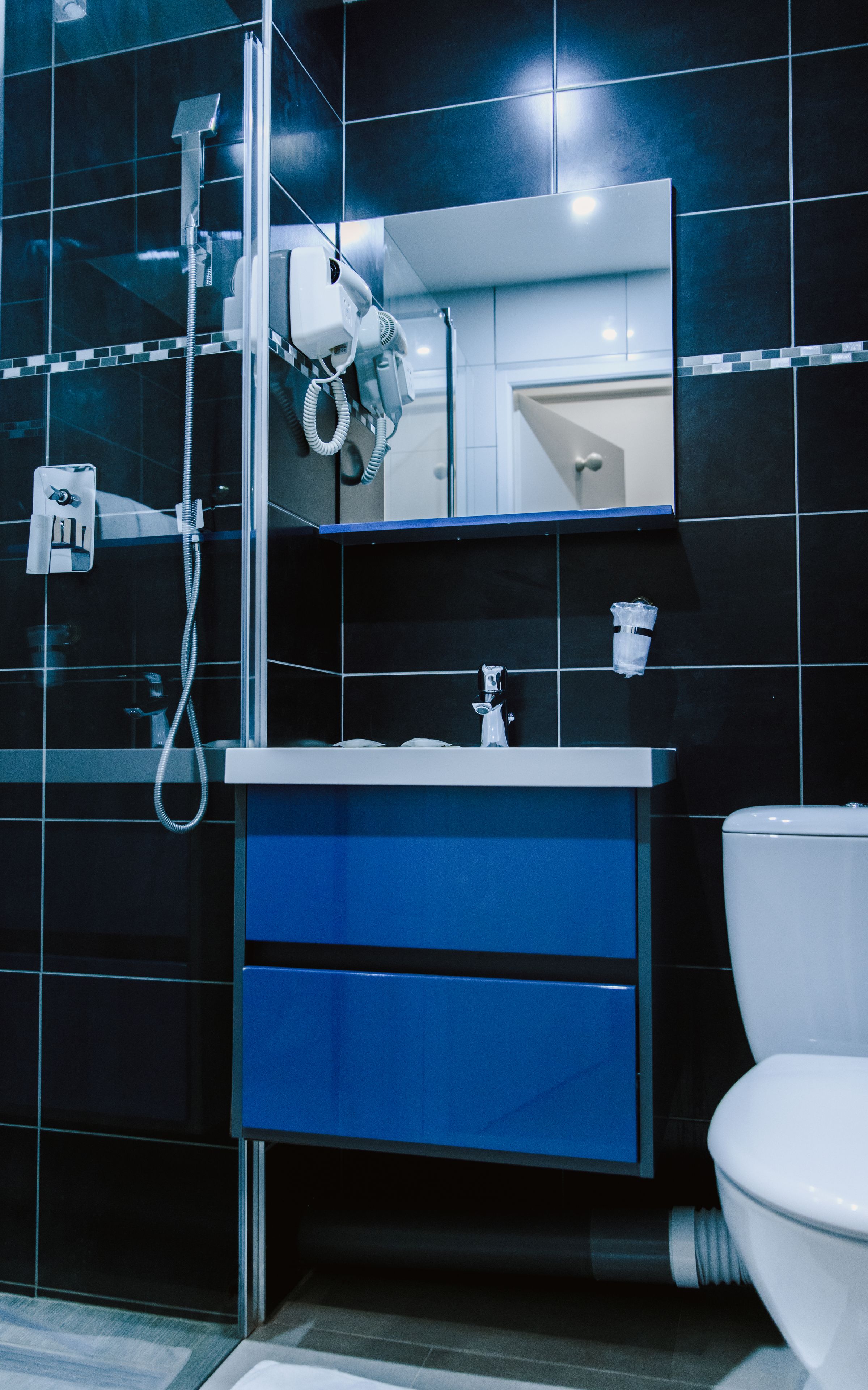 A modern bathroom with a glass-enclosed shower, a white toilet, and a blue vanity with a mirror.