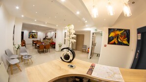 A modern hotel lobby with a wooden reception desk, seating area, and a dining space. - Hotel des Arcades (Reims)