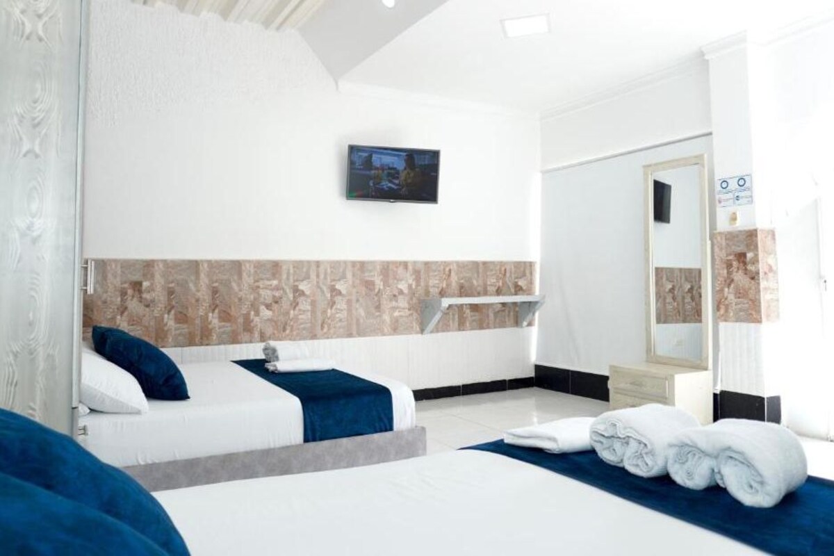 A hotel room with a large bed, a TV mounted on the wall, and a bathroom with a mirror and towel rack.