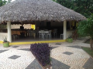 A thatched-roof outdoor dining area with tables and chairs, surrounded by a paved walkway and potted plants. - Hotel Villas del Mar (Pedernales)