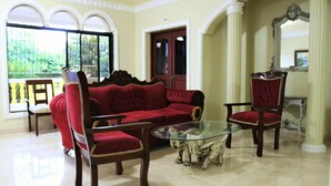 Una habitación con un sofá rojo, dos sillas rojas, una mesa de centro de vidrio y vistas a través de amplios ventanales.