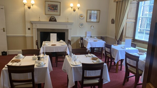 A dining area with tables set for four, a fireplace, and framed artwork on the walls. - Orchard Club - Newton House (Knaresborough)