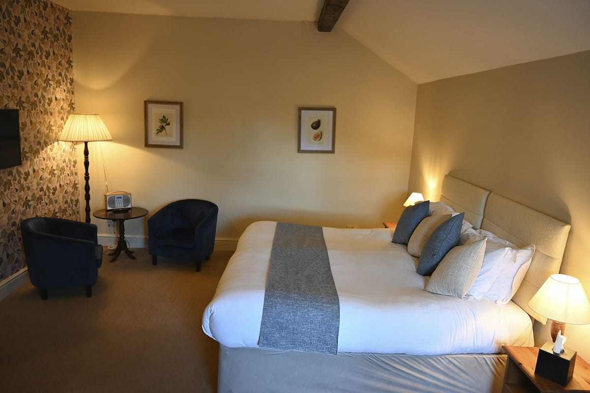 Ein Hotelzimmer mit einem großen Bett, zwei Sessel, einem kleinen Tisch und zwei Wandleuchten.