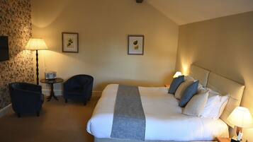 A hotel room with a large bed, two chairs, a small table, and two wall-mounted lamps.