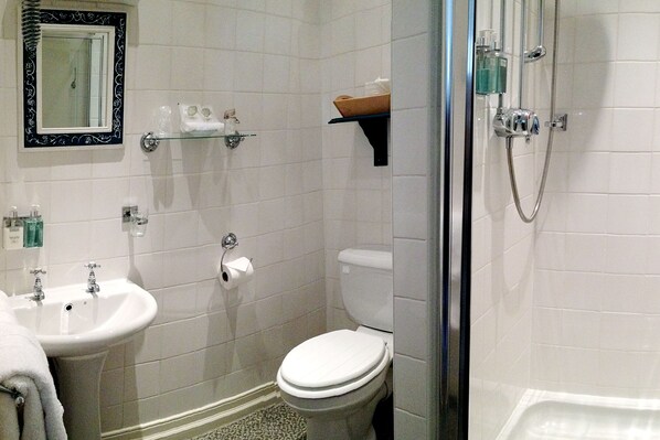 A bathroom with a sink, toilet, and shower. There are shelves with toiletries and a mirror above the sink. - Orchard Club - Newton House (Knaresborough)