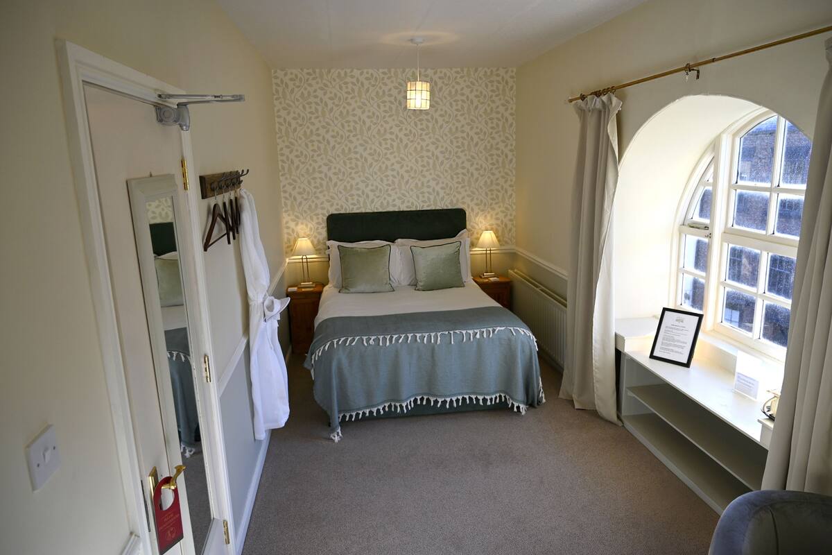 Ein Schlafzimmer mit Bett, Nachttischlampen, einem Fenster mit Aussicht, einem Spiegel und einer Tür mit Handtuchhalter.
