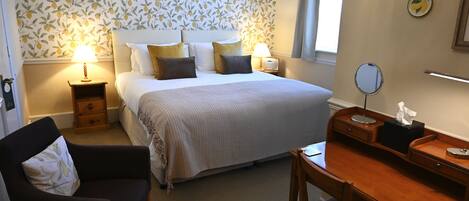 A neatly arranged bedroom with a bed, bedside tables, a desk, and a chair.