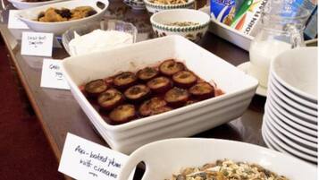 Buffet com diversos pratos, incluindo maçãs assadas com canela, granola e opções de cereais.