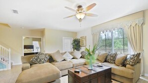 A living room with a ceiling fan, two sofas, a coffee table, and a large window with curtains. - Calabria (Kissimmee)