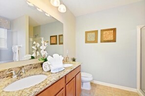 Un baño con encimera de granito, dos lavamanos, un espejo grande y obras de arte enmarcadas en la pared.
