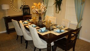 A dining room with a dark wooden table set for six, surrounded by white upholstered chairs. - Calabria (Kissimmee)
