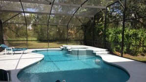 A swimming pool with a curved design, surrounded by a covered patio area with lounge chairs and a table. - Doral Woods (Kissimmee)