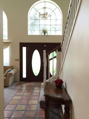A hallway with a wooden bench, a flower vase, and a large arched window with a chandelier.