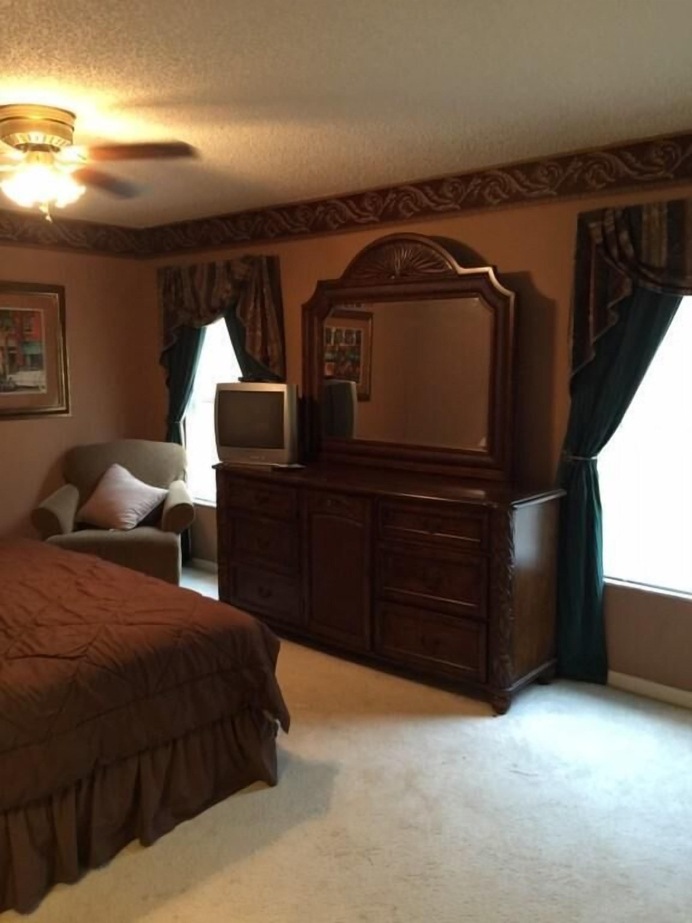 Een slaapkamer met een groot bed, een dressoir, een stoel, een televisie en een plafondventilator.