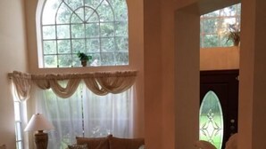 A living room with a large arched window, a sofa, a coffee table, and a statue. - Doral Woods (Kissimmee)
