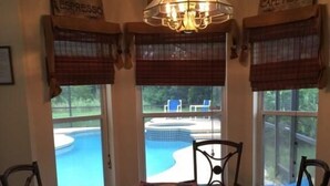 A dining area with a glass table and chairs, a chandelier, and windows with blinds. - Doral Woods (Kissimmee)