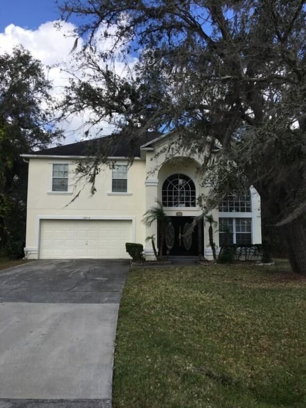 A two-story house with a garage, a large arched entrance, and a lawn.