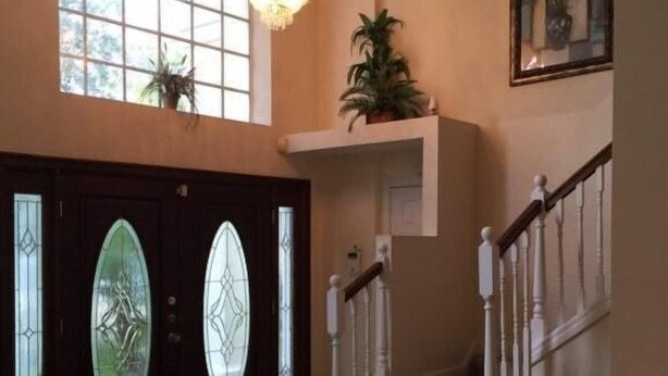 A spacious foyer with a grand staircase, a chandelier, and a large arched window. - Doral Woods (Kissimmee)