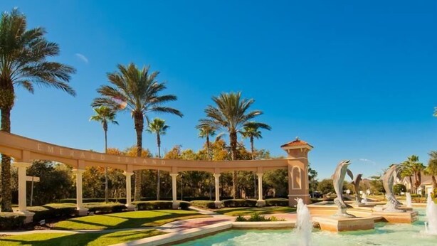 Uma área de piscina com piscina azul cristalina, uma pérgola com a sinalização 'Emerald Island', palmeiras e uma fonte.