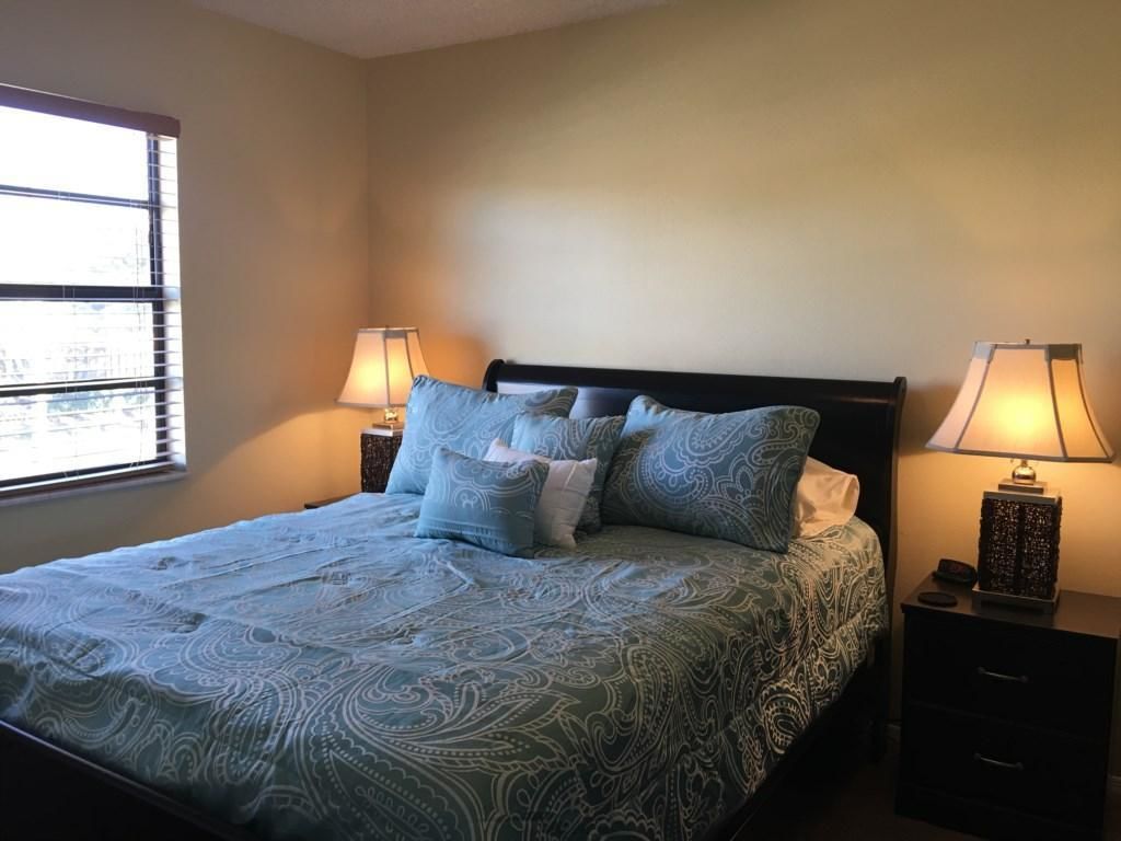 A neatly made bed with patterned bedding, two bedside lamps, and a window with blinds.