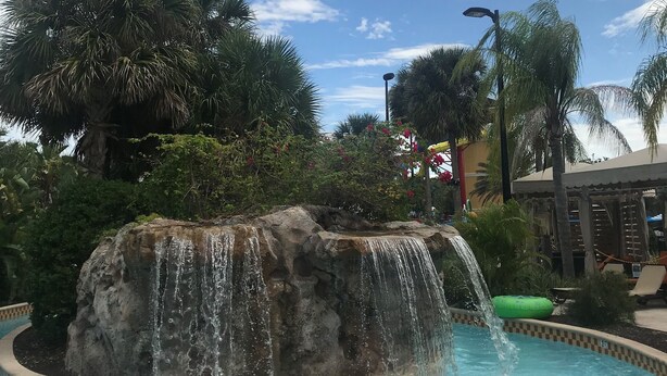 Een zwembad met een waterval, omringd door palmbomen en een heldere lucht.