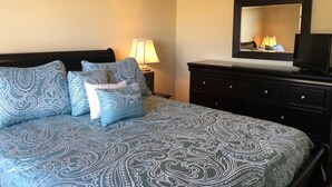 Een slaapkamer met een bed, een dressoir, een spiegel en een televisie.