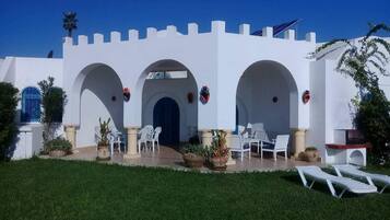 A white building with three arches, outdoor seating, and potted plants.