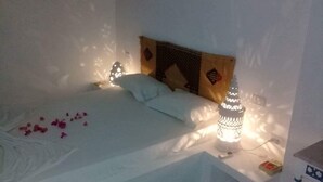 A bed with white linens, a decorative headboard, and two wall-mounted lamps. - Maamoura Beach House (El Maâmoura)