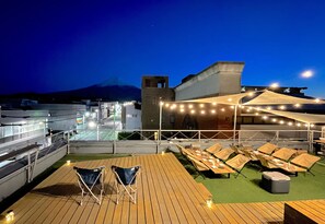 Una terraza en la azotea con sillones, mesas, luces colgantes y vistas a la montaña.