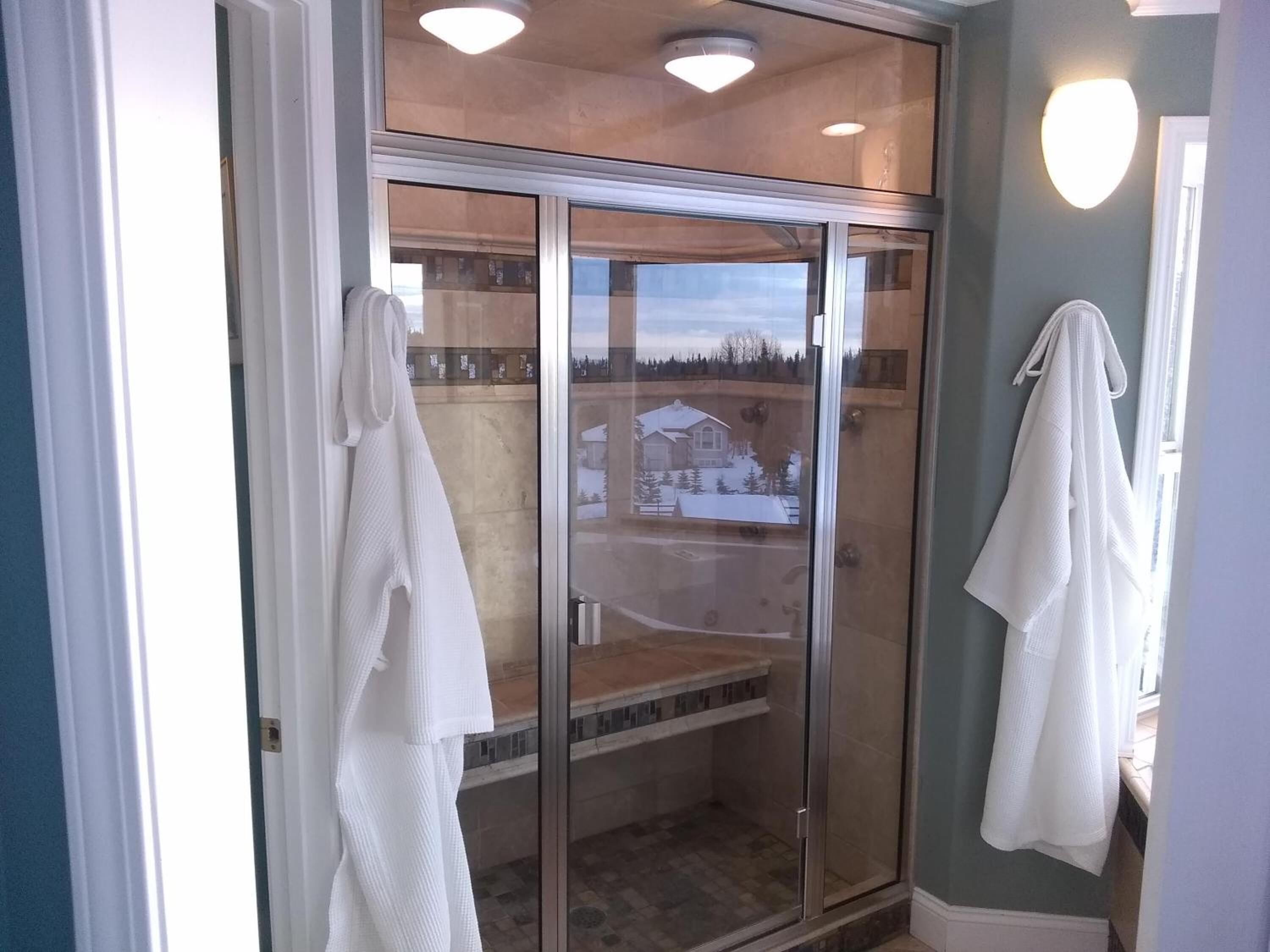 A glass-enclosed shower area with a view of a snowy landscape, a bench, and two white towels hanging on the wall.