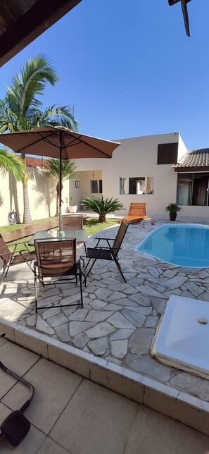Uma área de pátio com piso de pedra, mobiliário de exterior, piscina e palmeiras.
