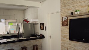 A modern kitchen with a built-in refrigerator, a dining area with stools, and a television mounted on a textured wall. - Casa com piscina em Caraguatatuba (Caraguatatuba)