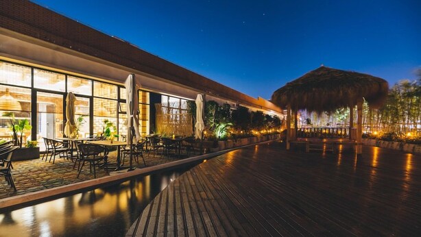 Ein Nachtblick auf einen Resort-Außenbereich mit Pool, Holzterrasse und einem strohgedeckten Gebäude.