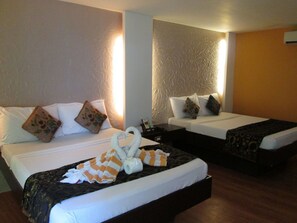 Habitación de hotel con dos camas, cada una con ropa blanca y almohadones decorativos. En la cama del primer plano, hay un arreglo de toallas con forma de corazón.