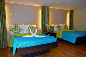 Una habitación de hotel con dos camas, cada una con una colcha azul y almohadas blancas con un estampado verde. En la cama del primer plano, hay un cisne decorativo hecho con toallas.
