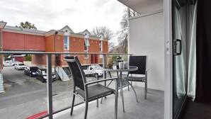 A balcony with a glass railing, two chairs, a small table, and a potted plant. - Armagh Apartment 3 - Central Christchurch (Christchurch)