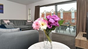 A living room with a grey sofa, a round marble table with a vase of flowers, and a large window with a view of buildings. - Armagh Apartment 3 - Central Christchurch (Christchurch)