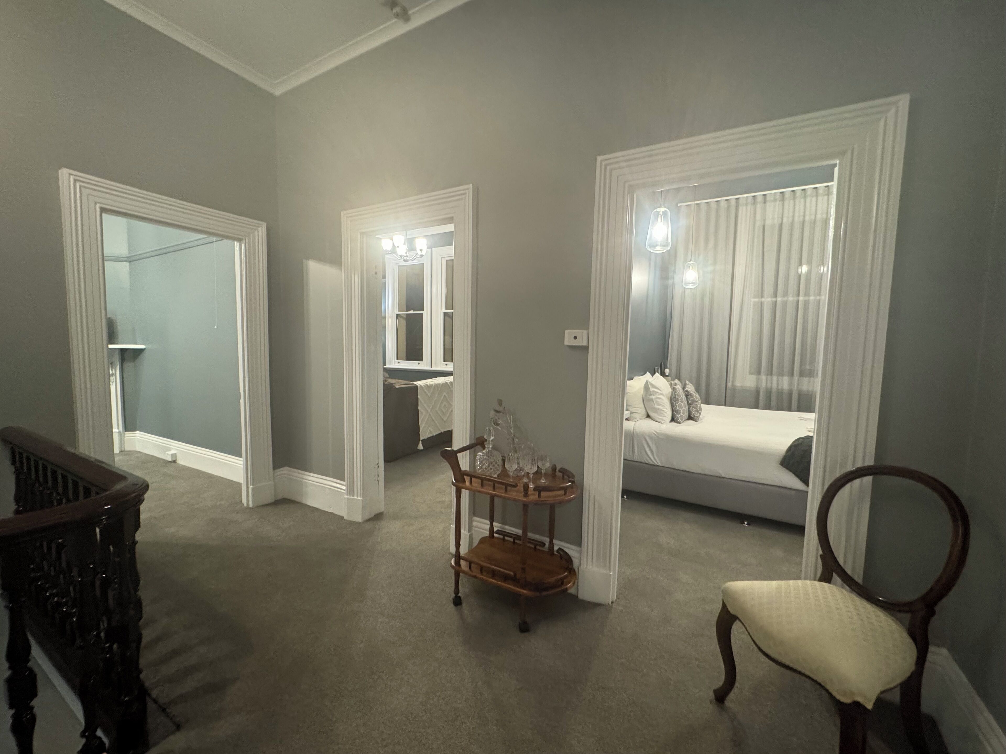 A bedroom with a bed, a chair, a small table with a vase, and a mirror.